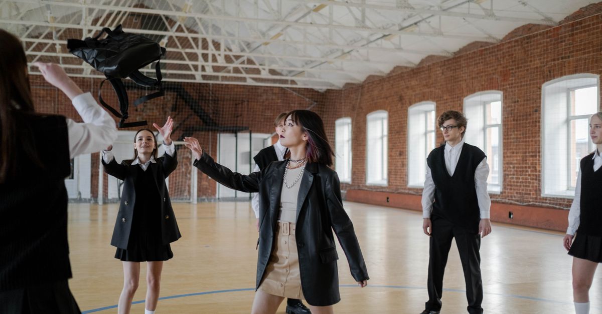 High school students in uniforms throwing a backpack in a gym, showcasing youth camaraderie.